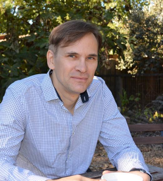 A man wearing a light colored collared shirt in front of greenery