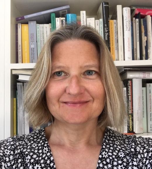 A woman with light hair in front of a bookshelf