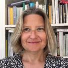 A woman with light hair in front of a bookshelf